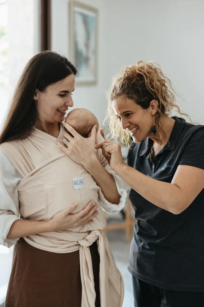 Silvia smiles with a mother holding her baby in a fabric wrap.