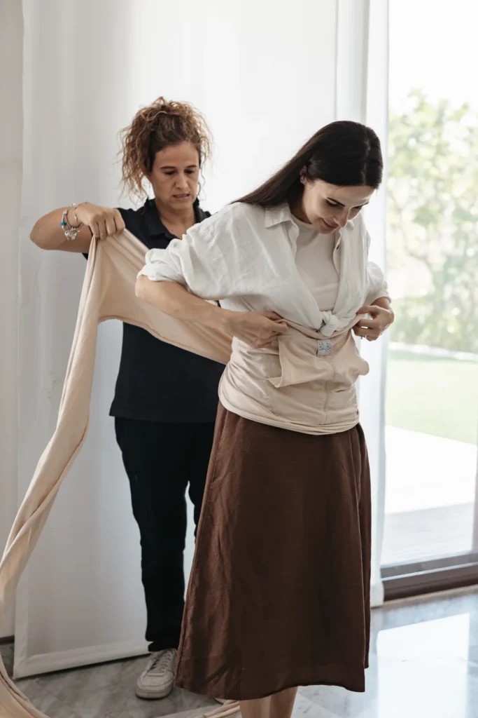 Silvia helps a mother adjust a fabric wrap around her waist.