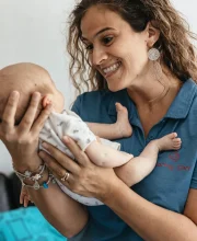 Silvia smiles as she gently supports a baby in her hands.